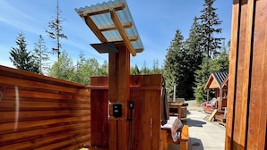 A wooden cabin with a covered outdoor seating area, a stone pathway, and a view of the surrounding forest.