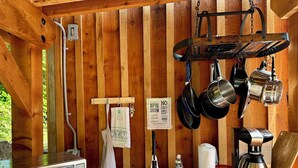 A rustic kitchen with wooden walls, a stainless steel sink, hanging pots, a kettle, a toaster, and a sign about a septic system.