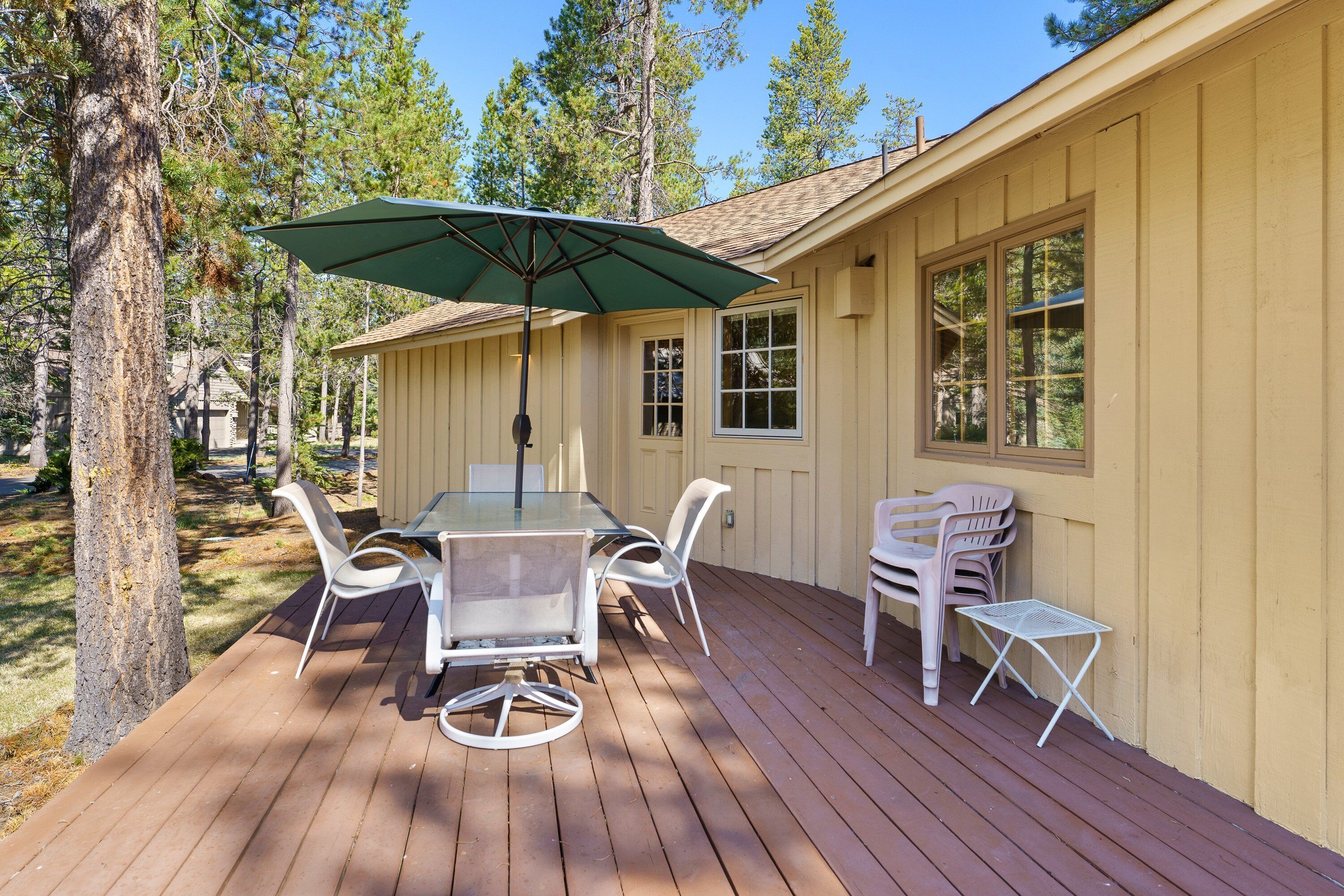 A wooden deck with a glass table and chairs, an umbrella, and a small table.