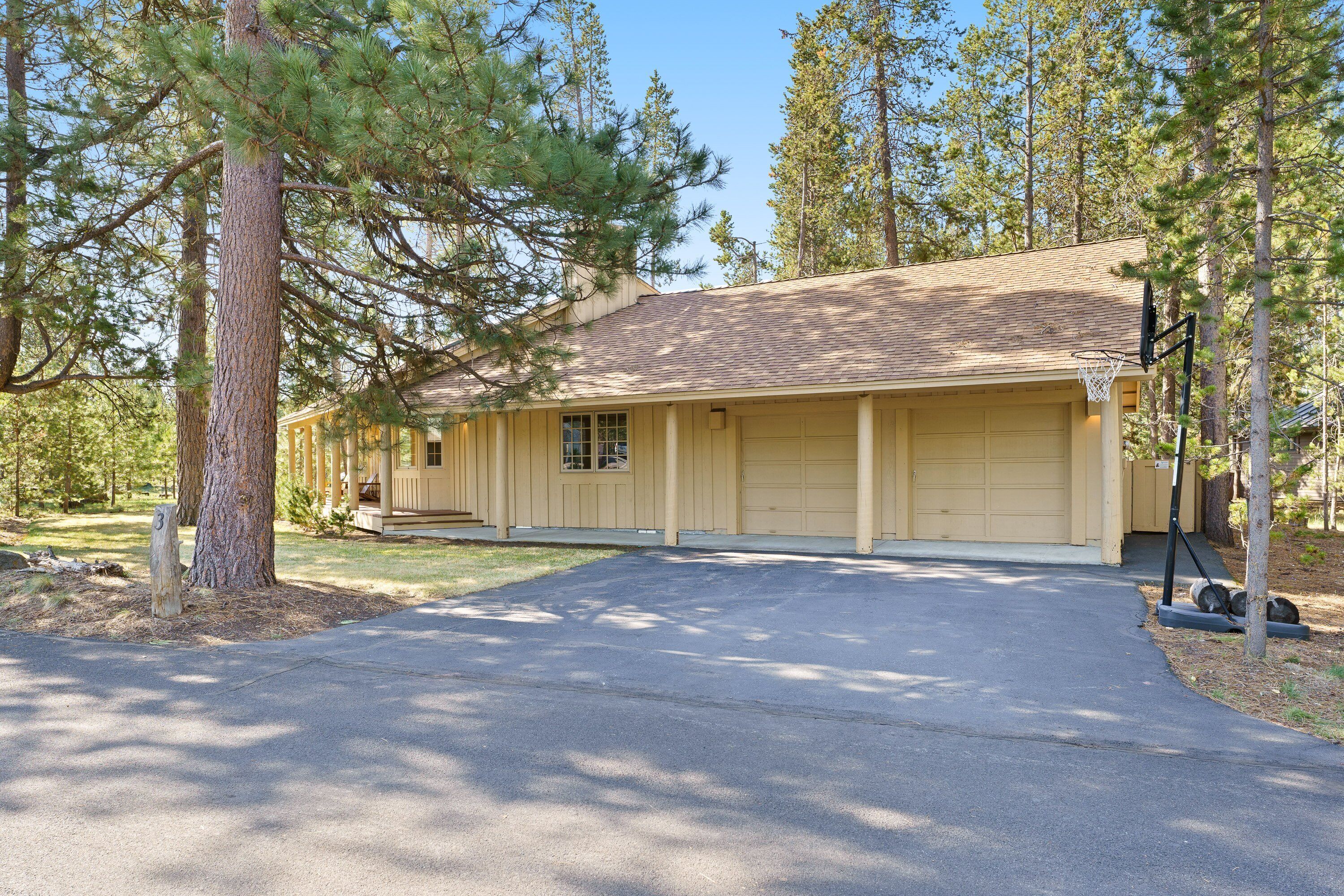 A two-story house with a garage, surrounded by tall pine trees.