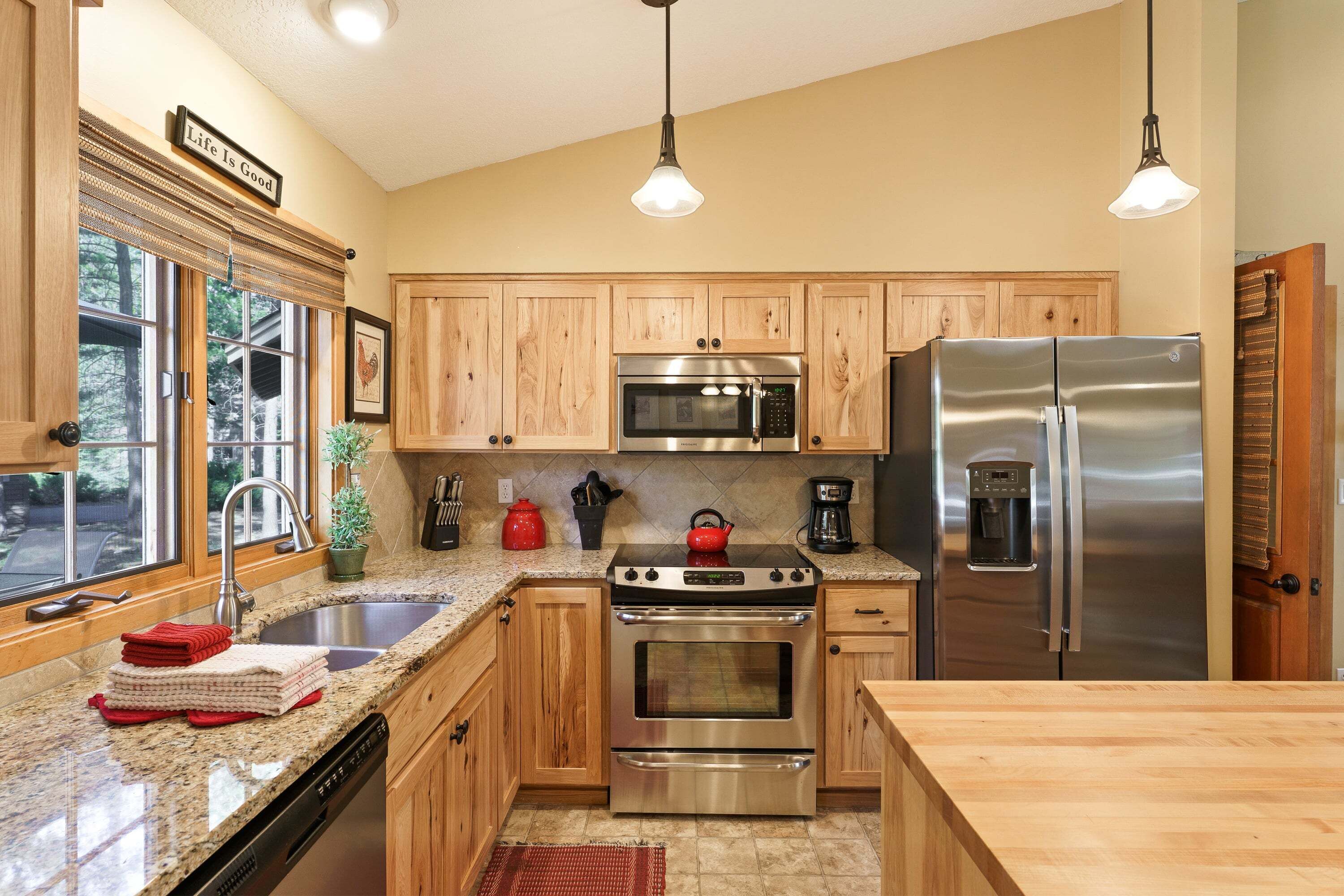 A kitchen with wooden cabinets, stainless steel appliances, granite countertops, and a window with blinds.