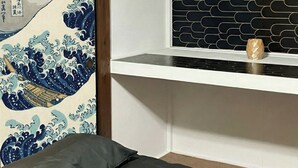 Ett rum med en traditionell japansk vägg dekorerad med ett vågmönster, en vit hylla med en svart, geometrisk bakgrund och en liten dekorativ prydnad på hyllan.