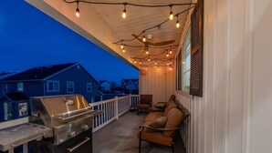 Un espace extérieur abrité, équipé d’un barbecue, de sièges et de guirlandes lumineuses.