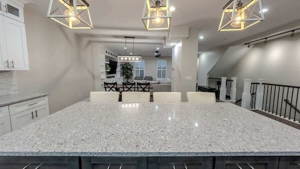 Une cuisine moderne dotée d’un grand îlot central, de luminaires suspendus et d’un escalier.