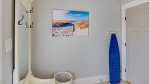 Een badkamer met een schilderij van een zandstrand, een blauw douchegordijn en een witte emmer.