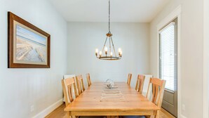 A dining room with a wooden table, six chairs, a chandelier, and a framed picture on the wall. - 404a The Hilltop House (Virginia Beach)