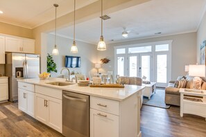 Una cocina moderna con una isla central, electrodomésticos de acero inoxidable, iluminación colgante y vistas al salón.