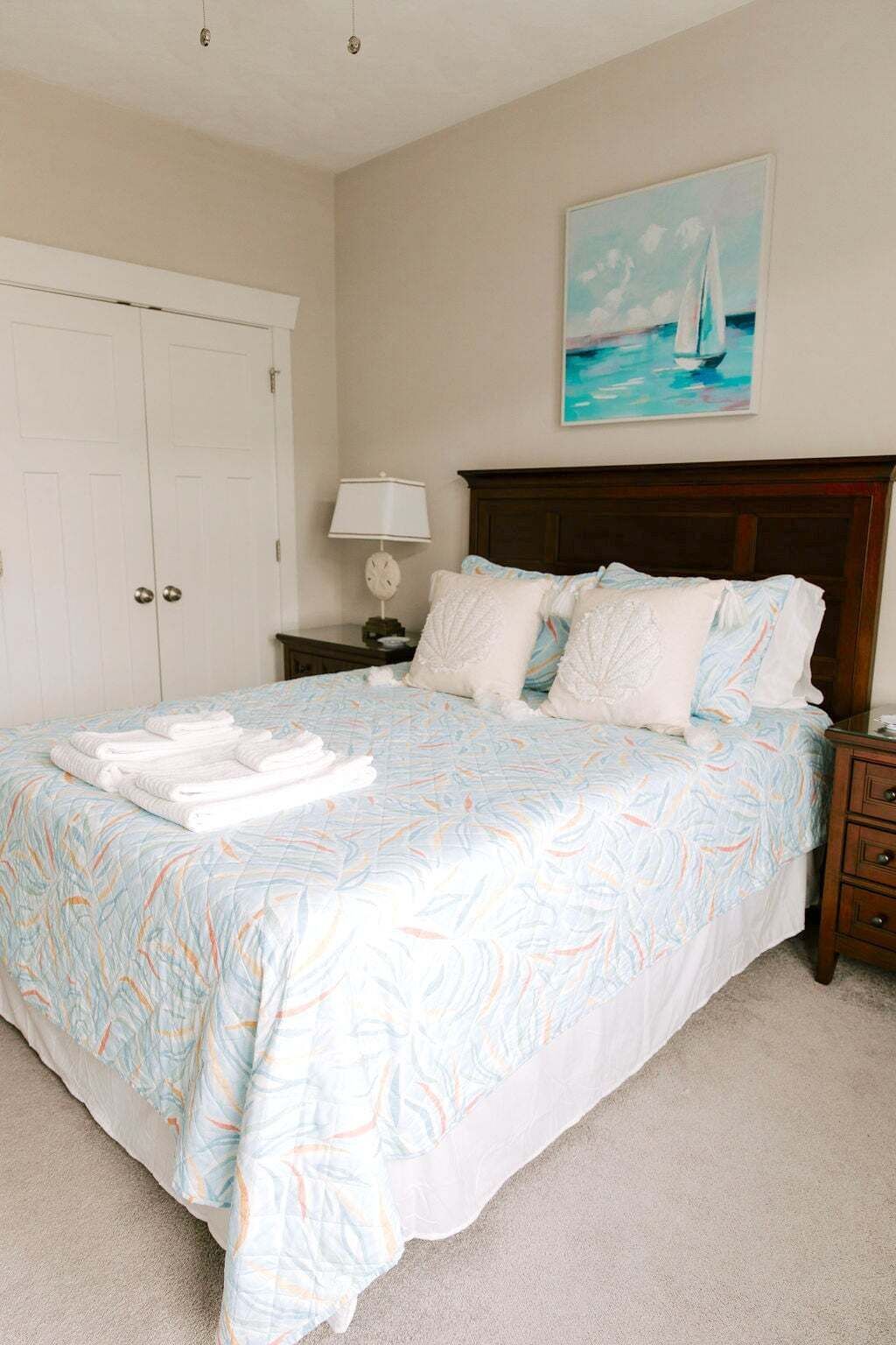 A bedroom with a bed, a nightstand, a lamp, a painting, and a door.