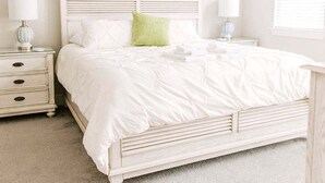 Ein Schlafzimmer mit einem weißen Bett, zwei Nachttischen, einem Deckenventilator und einem Fenster mit Jalousien.