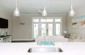 Une cuisine avec un plan de travail blanc, un évier et trois luminaires suspendus.