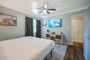 A bedroom with a bed, a ceiling fan, a TV mounted on the wall, a small plant on a side table, and a door leading to another room. - 4297 Earney Rd, Unit 2, Woodstock (Woodstock)