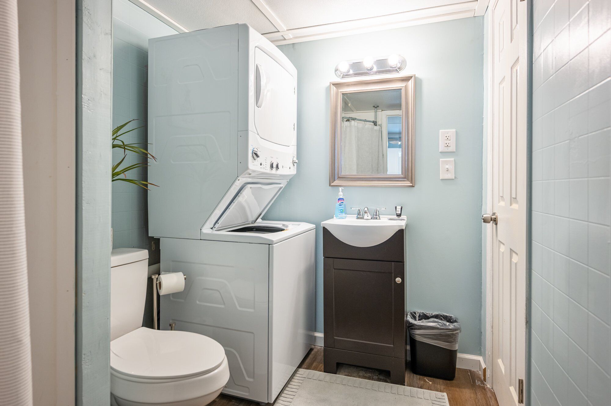 Ein kleines Badezimmer mit Waschmaschine, Toilette, Waschbecken und Spiegel.