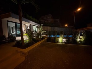 Una casa moderna con piscina, rodeada de jardines bien iluminados.