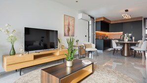 Un salon moderne doté d’un téléviseur à écran plat, d’un meuble de rangement en bois et d’une table basse. On y trouve également un coin repas avec une table ronde et des chaises.
