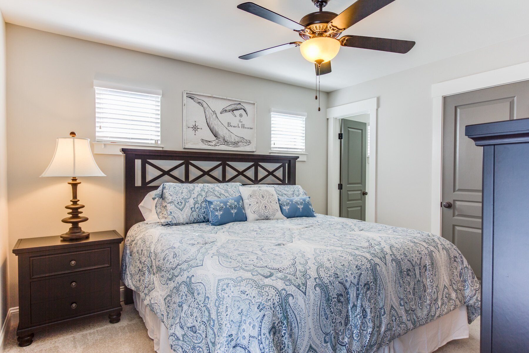 A bedroom with a bed, a nightstand, a lamp, a ceiling fan, and a door.