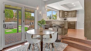 A modern kitchen with a central island, sliding glass doors leading to a patio, and a dining area with a round table and chairs. - 49th St (Scottsdale)