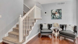 A staircase with white railings and carpeted steps, two leather sofas with patterned cushions, and a wall-mounted artwork. - 49th St (Scottsdale)