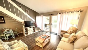 A living room with a wooden floor, a sofa, a coffee table, a TV, and a staircase. - 601 Double Eagle Trace (Seabrook Island)