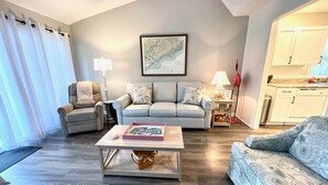 A living room with a sofa, armchairs, a coffee table, and a kitchen area. - 601 Double Eagle Trace (Seabrook Island)
