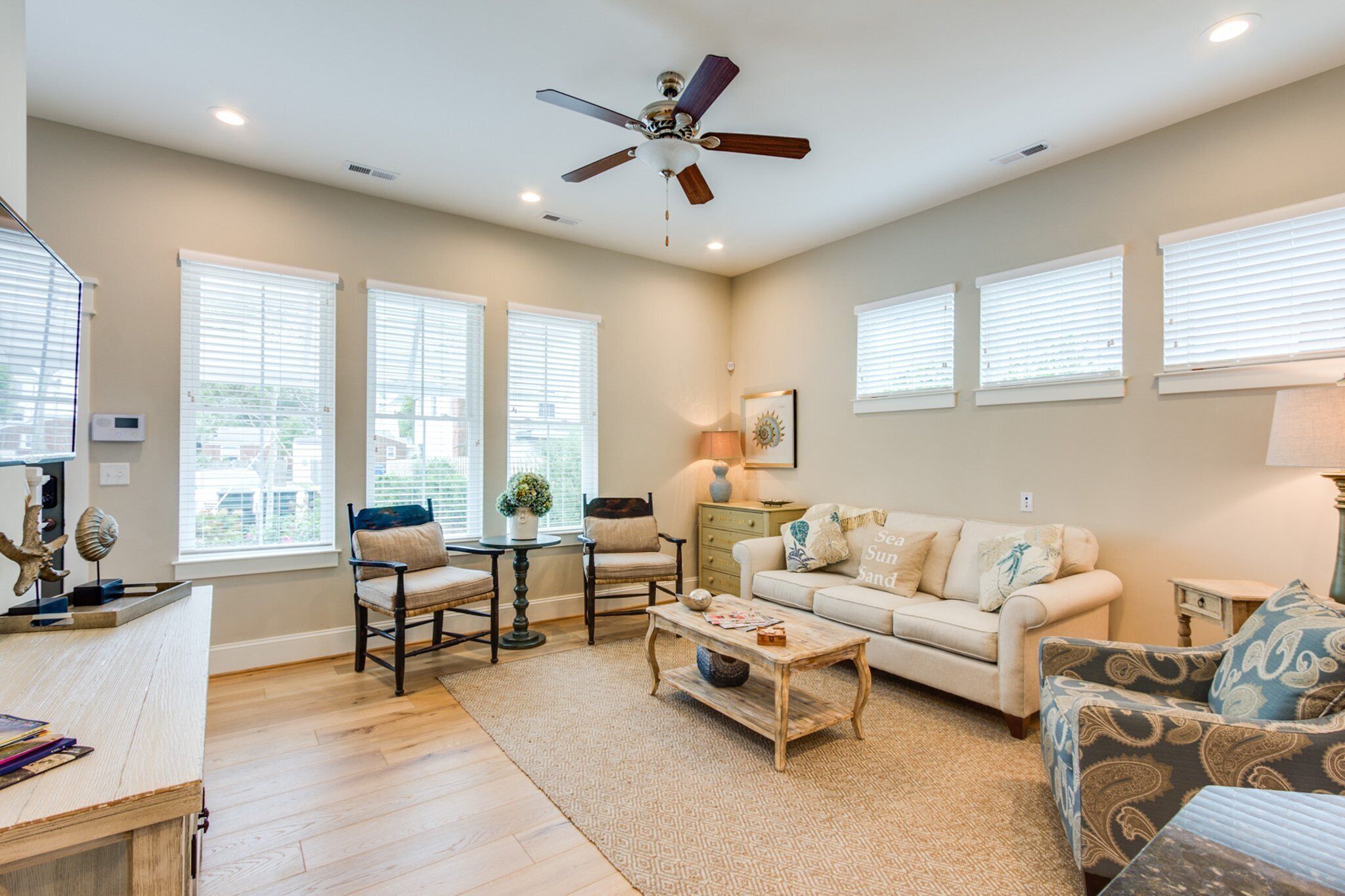 A spacious living room with a ceiling fan, a sofa, a patterned armchair, a coffee table, and a dining table with chairs.