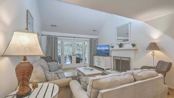 A living room with a sofa, a coffee table, a lamp, a television, a fireplace, and a large window.