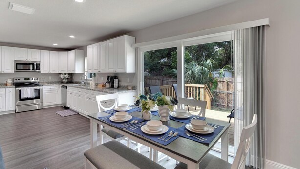 A modern kitchen with white cabinets, stainless steel appliances, and a dining area with a table set for four. - 6506 N 22nd St (Tampa)