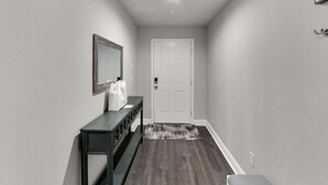 A hallway with a dark wood floor, a white door, a bench, a console table, and a patterned rug. - 6506 N 22nd St (Tampa)