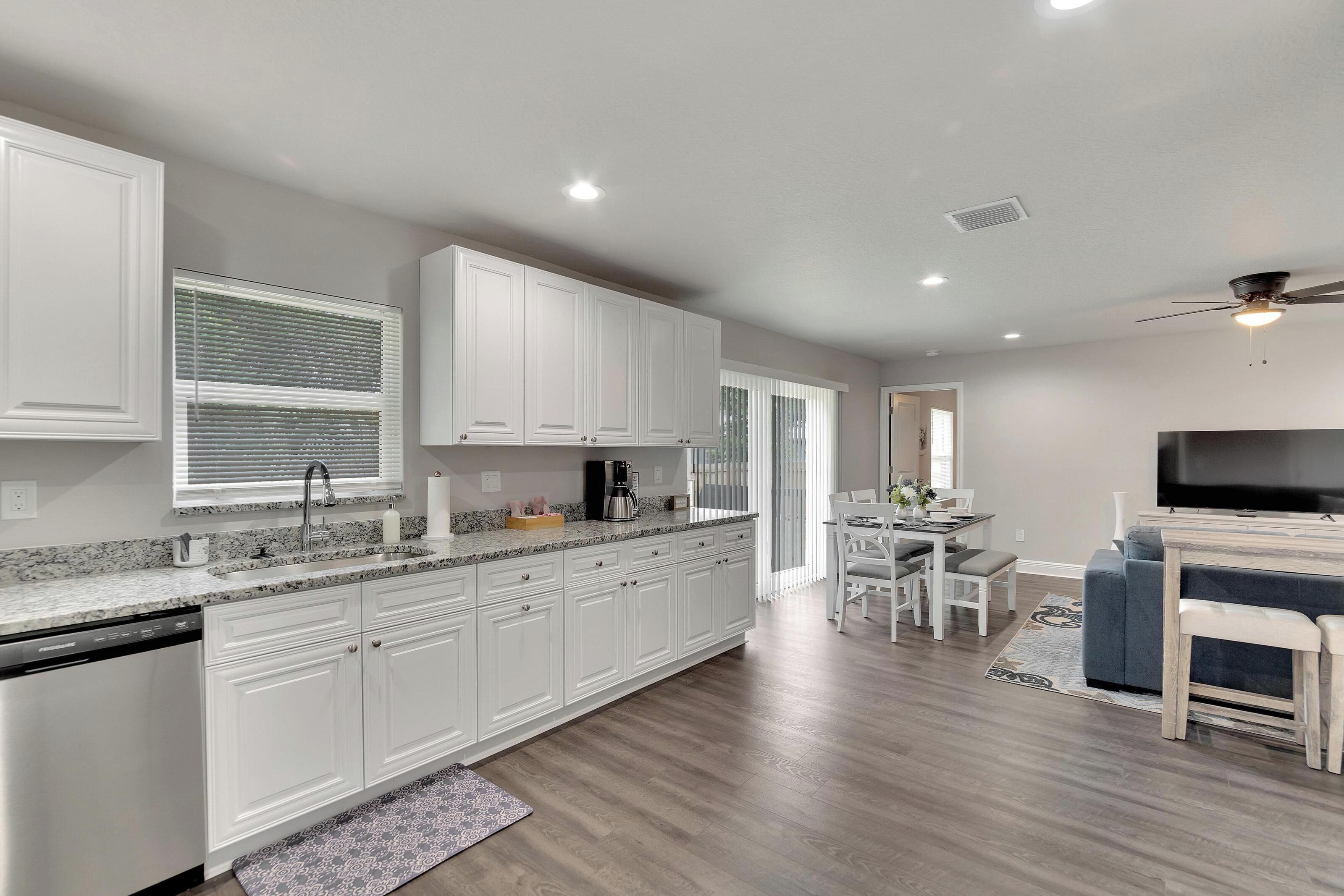 A modern kitchen with white cabinets, a built-in dishwasher, and a dining area with a TV and seating.