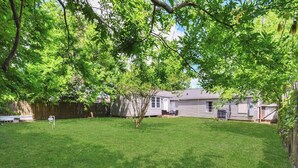 A backyard with a lawn, a tree, and a house. - 5BR 3BA Home With Hot Tub Near Stadiums & Airport (Houston)