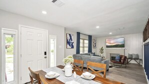 A dining area with a wooden table set for four, a gray placemat, and a white vase with flowers. - 5BR 3BA Home With Hot Tub Near Stadiums & Airport (Houston)