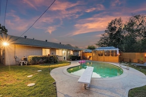 A backyard with a swimming pool, a wooden deck, and a house with a brick exterior. - 4BR 2B Home With Pool, Hot Tub, Fire Pit (Irving)