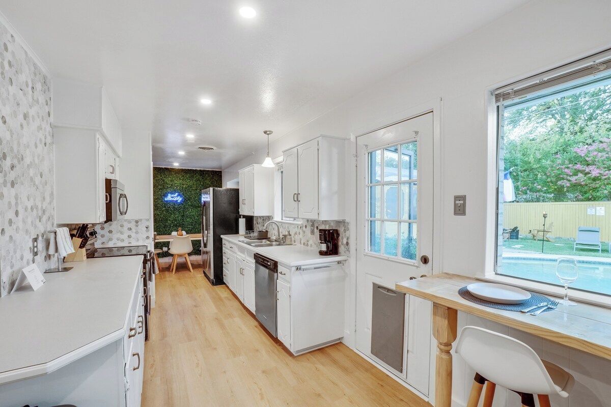 A modern kitchen with white cabinets, a dishwasher, and a dining area with a table and chairs.