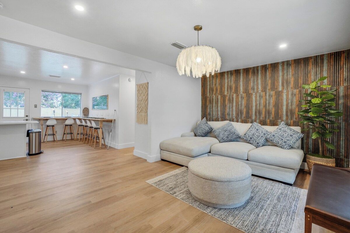 A modern living room with a sofa, ottoman, and a hanging light fixture.