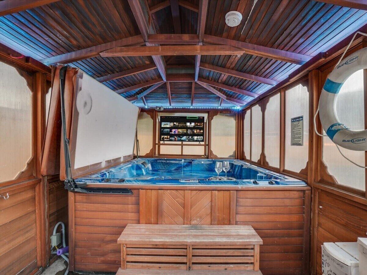 Interior em madeira com banheira de hidromassagem, um banco de madeira e painel de controle com vários botões e telas.