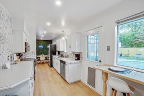 Una cucina moderna con mobili bianchi, lavastoviglie e zona pranzo con tavolo e sedie.