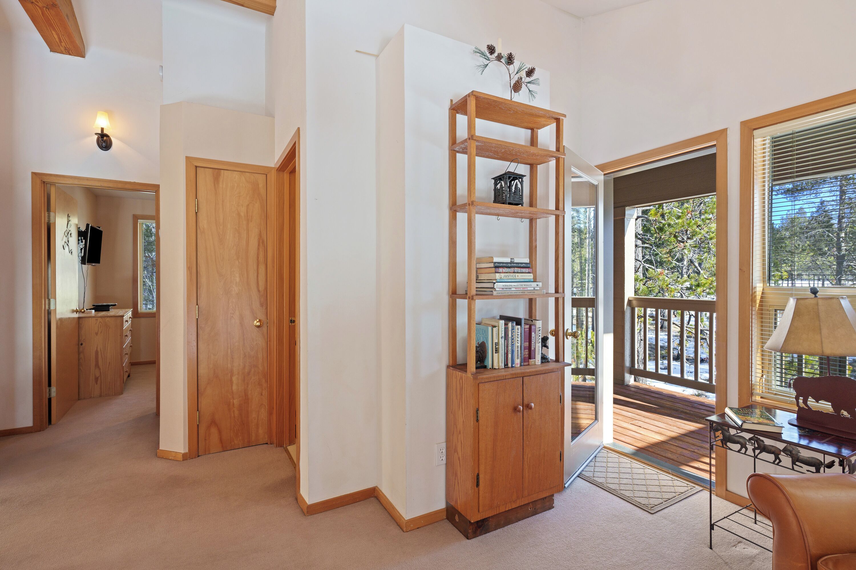 A room with a wooden bookshelf, a desk with a lamp, and a view of the outdoors through a large window.