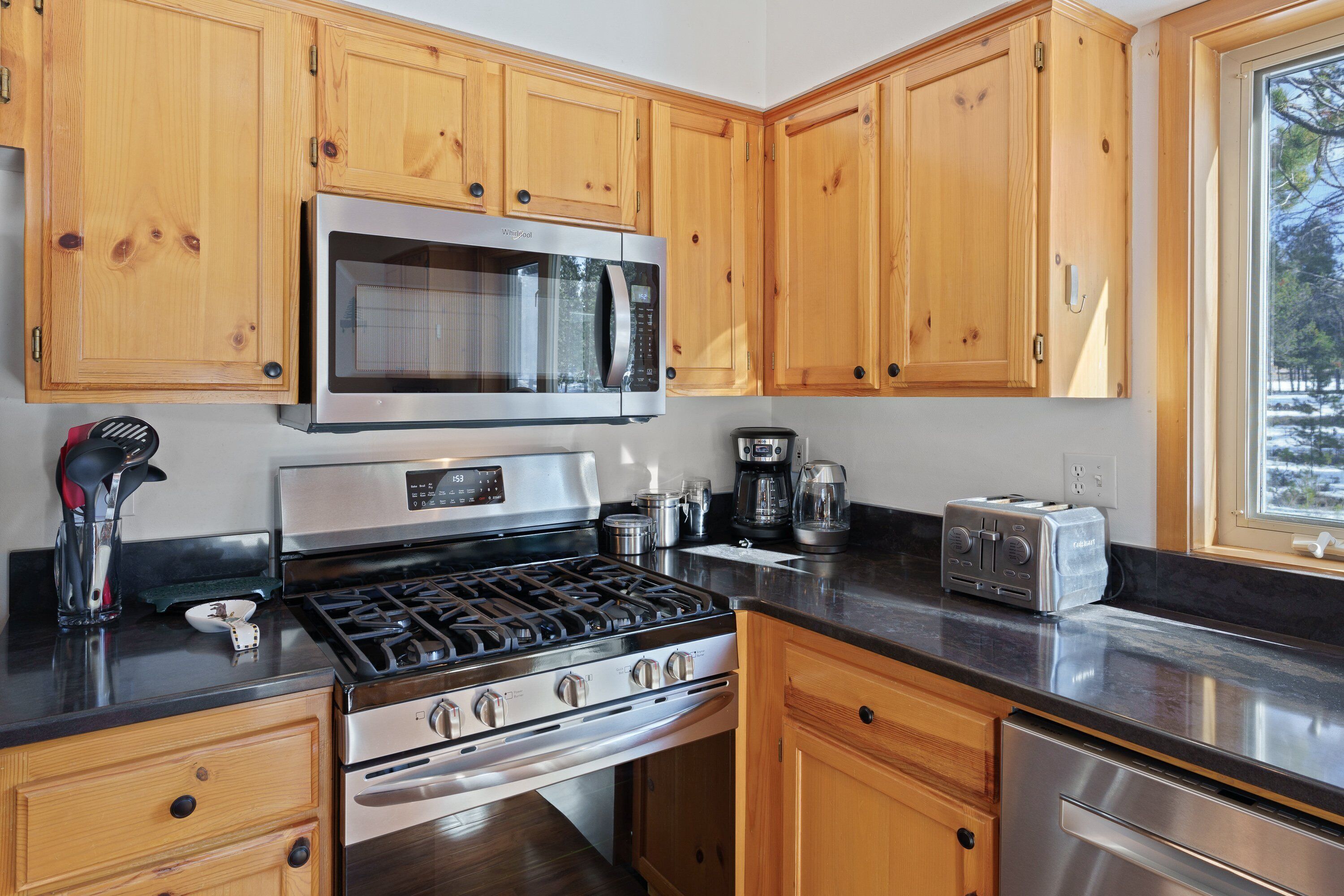 Een moderne keuken met houten kastjes, roestvrijstalen apparatuur en een raam dat voor natuurlijk licht zorgt.