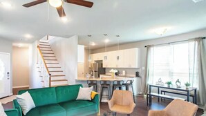 Um apartamento moderno com sofá verde, área de jantar, cozinha e escada.