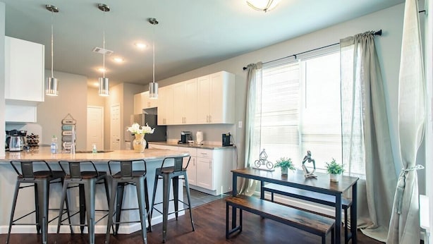 Cozinha moderna com ilha central, banquetas, luminárias pendentes e mesa de jantar com banco.