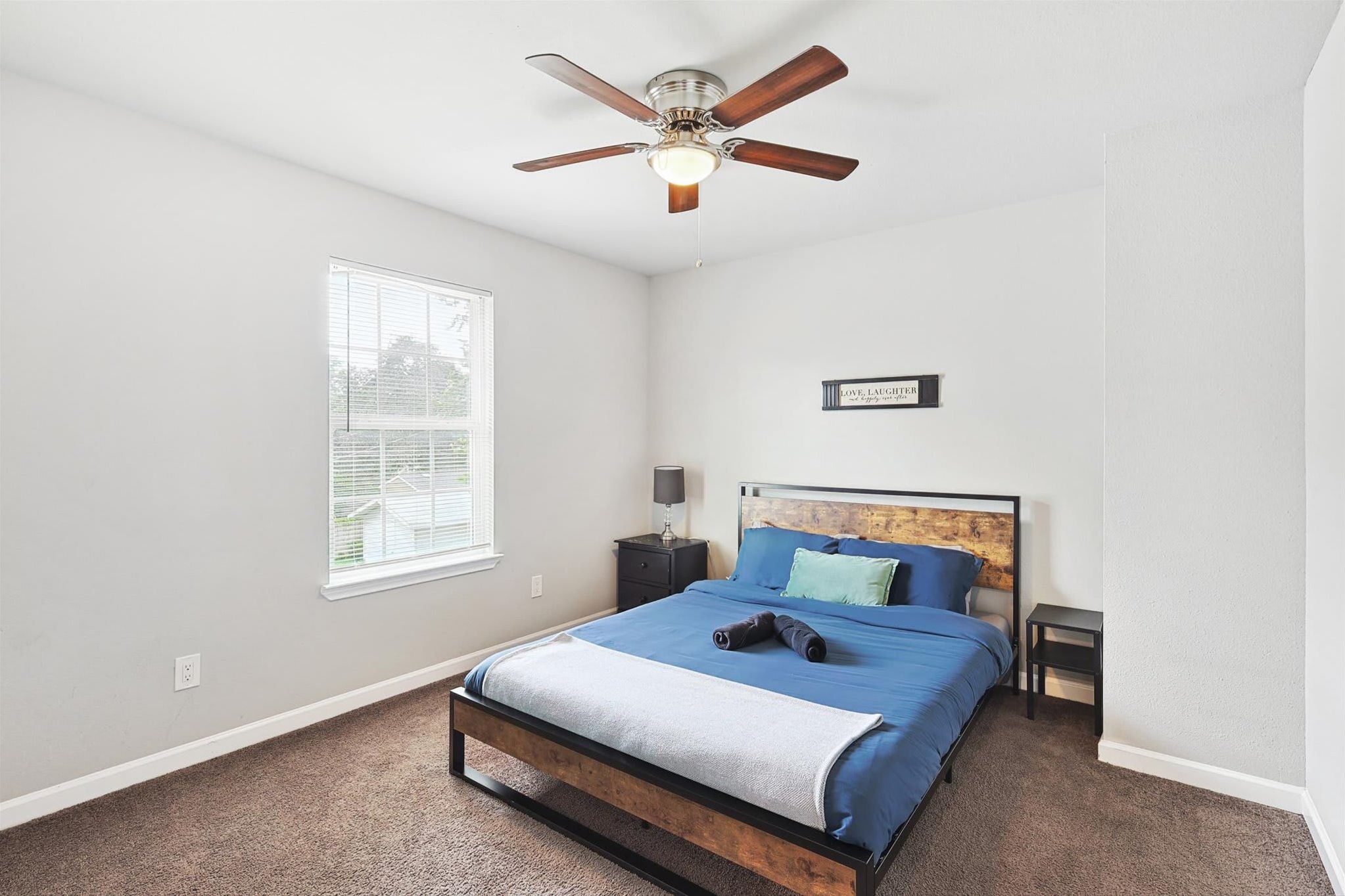 A bedroom with a bed, a ceiling fan, a nightstand, a window, and a wall-mounted sign.