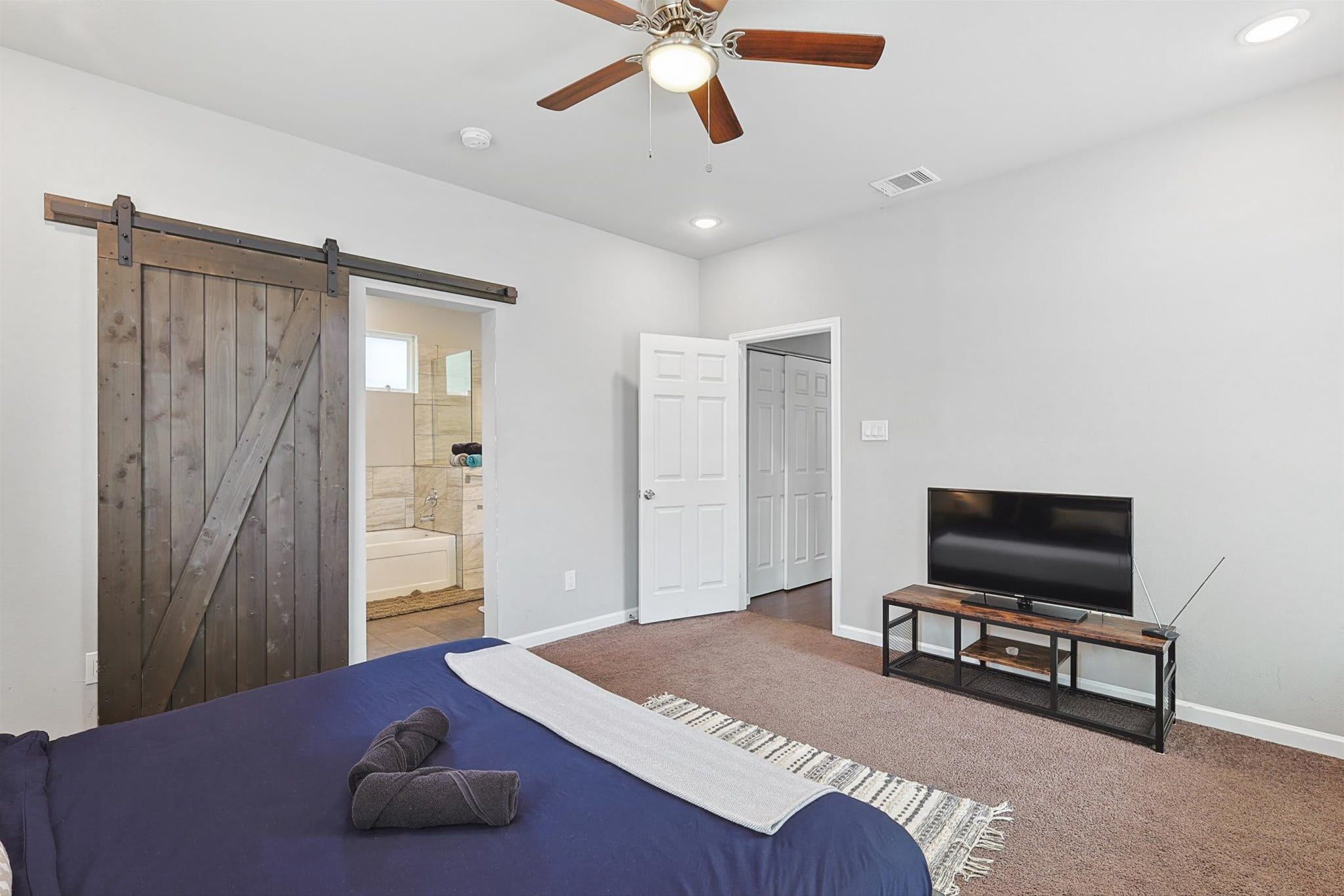 A bedroom with a bed, a TV, a ceiling fan, and a sliding barn door.