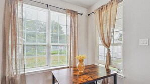 Um quarto com uma mesa de madeira, cortinas bege e uma janela com persianas.