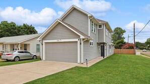 Um edifício residencial de dois andares com garagem, um carro estacionado em frente e um gramado bem cuidado.