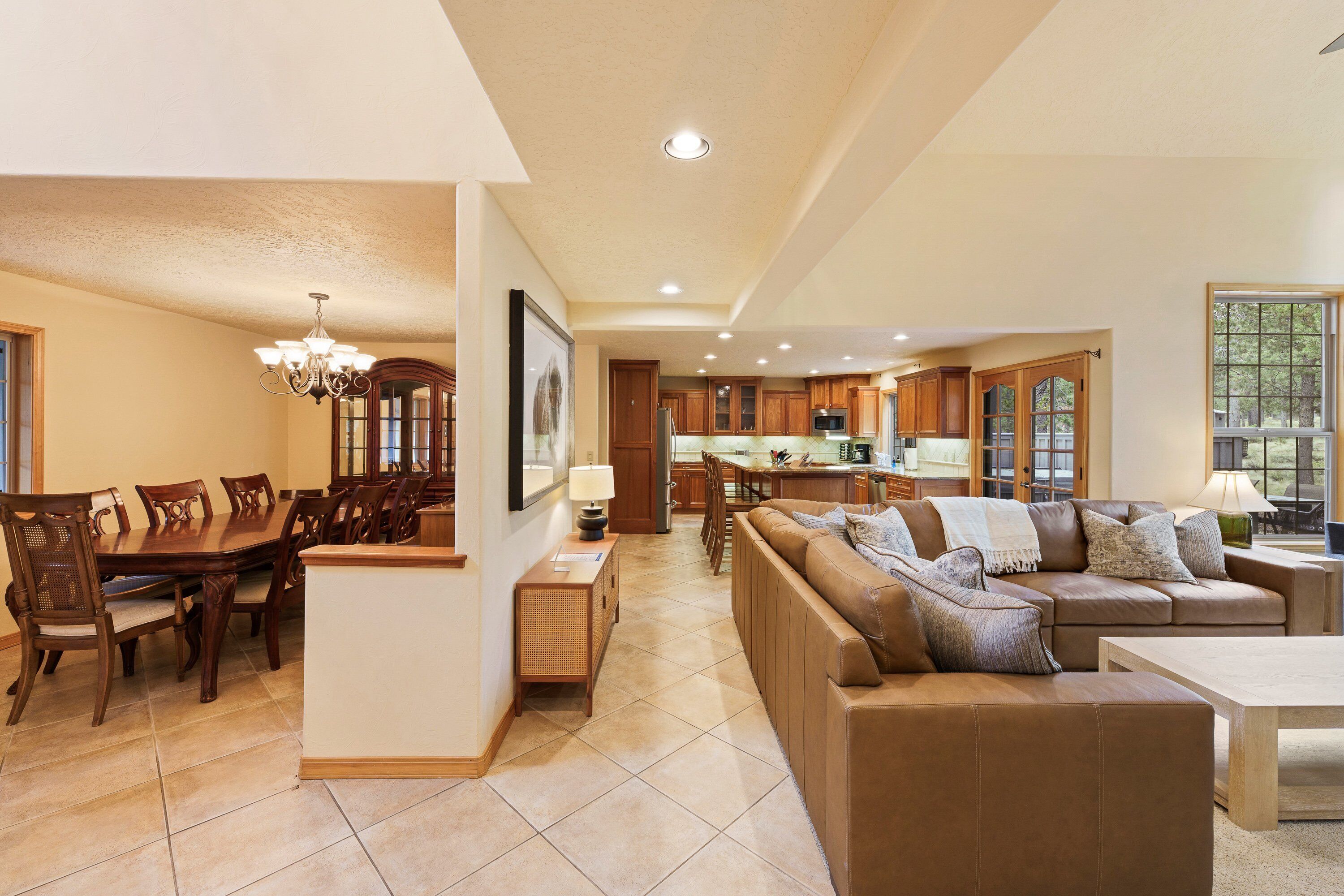 A spacious living area with a large brown leather sofa, a dining table with chairs, and a kitchen in the background.
