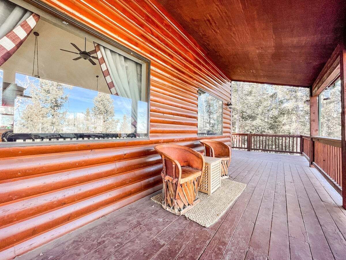 A log cabin with a wooden deck, two wicker chairs, and a ceiling fan.
