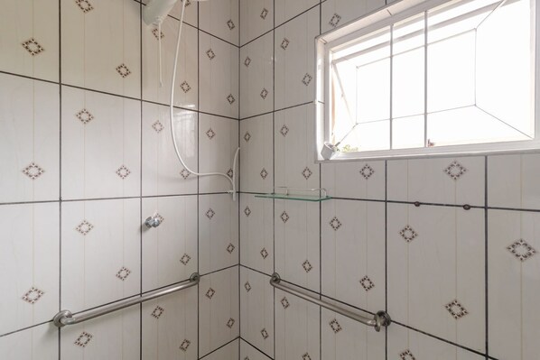 Une salle de bain avec des carreaux blancs, une fenêtre et une étagère en verre.