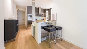 Een moderne keuken met een centraal eiland, roestvrijstalen apparatuur en zwarte barkrukken.