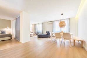 A modern living room with a sofa, dining table, and chairs. There is a bed in the background and a large window with curtains. - The Double Loft Designer Loft for 4 Next to Atocha (Madrid)