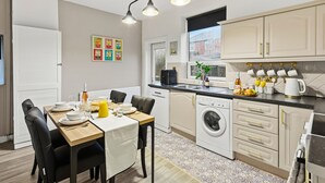 A modern kitchen with a dining area, featuring a washing machine, a coffee maker, and a fruit bowl on the counter. - Contractor or Corporate- 2 Bedroom Home | Office| Sleeps 6| Bills Inc (Bolton)