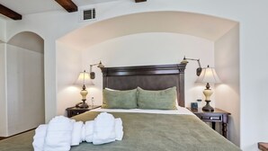 A neatly made bed with a green bedspread, two bedside lamps, and a pair of white towels on the bed.